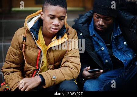 Zwei afrikanische männliche Freunde sitzen und am Telefon zusammen. Stockfoto