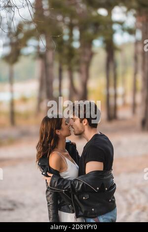 Seitenansicht des Mannes küssen und ausziehen Lederjacke Von Freundin im Wald Stockfoto