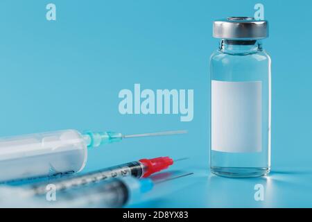 Fläschchen mit Impfstoffen und Spritzen in einer Reihe auf blauem Hintergrund Nahaufnahme. Stockfoto