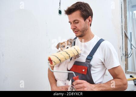 Mann mit Hund macht Renovierungsarbeiten im Zimmer. Gute Beziehung zwischen einem Hund und seinem Besitzer Stockfoto