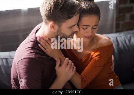 Besorgte Frau und junger Mann umarmen, während sie auf dem Sofa sitzen Stockfoto