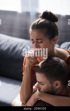 Weinende Frau, die die Faust in der Nähe des Mundes hält, während sie den geliebten Mann umarmt Stockfoto