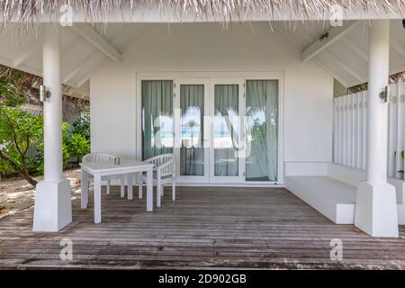 Luxusvillen am Strand. Moderne Holzterrasse, weiße Stühle und Tisch, tropischer Blick auf den Bungalow Stockfoto