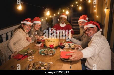 Glückliche ältere Freunde, die während des Weihnachtsessen zu Hause Selfie machen Tragen Santa Clause Hüte- Feiertage und Technologie Konzept - weich Fokus auf rechtes ma Stockfoto