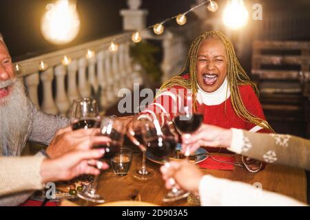 Mehrrassische Senioren feiern Silvester gemeinsam beim Abendessen Outdoor - Urlaub Konzept - Weiche Fokus auf afrikanische Frau Gesicht Stockfoto