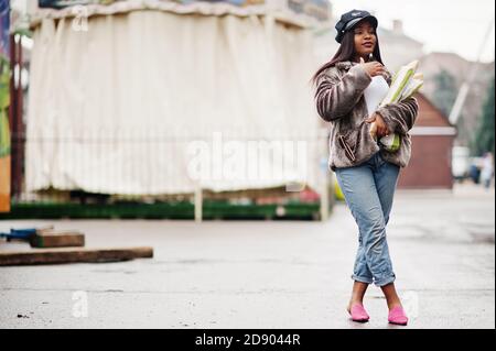 Modische afroamerikanische Frau in schwarzer Mütze und Fell mit zwei Baguette Rollen an den Händen. Stockfoto