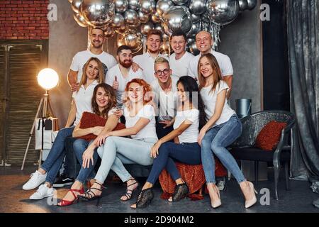 Fröhliche junge Leute feiern Neujahr in weihnachtlich dekorierten Zimmer Mit Beleuchtungsausrüstung Stockfoto