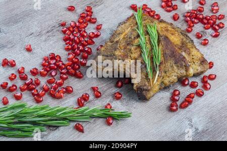 Gegrilltes Steak auf Holzgrund. Stück frittiertes Fleisch mit Granatapfelkernen und einem Zweig Rosmarin. Stockfoto