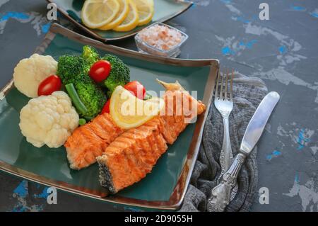 Diät Servieren von Lachs mit Zitrone, Brokkoli und Gemüse. Zwei Stücke gegrillter Lachs werden auf einem schönen Teller serviert Stockfoto