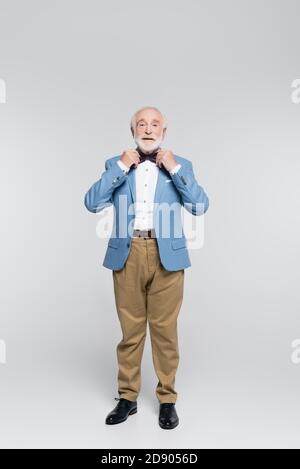 Lächelnder Senior Mann in Jacke Anpassung Fliege auf grau Hintergrund Stockfoto