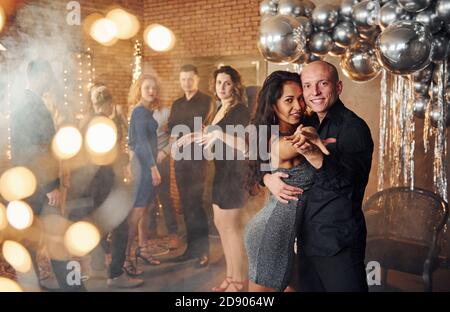Junge Paare tanzen gegen ihre Freunde in weihnachtlich dekorierten Raum Und feiern das neue Jahr Stockfoto