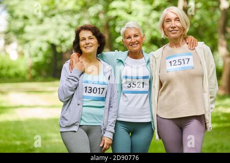Gruppe von drei fröhlichen älteren Freundinnen, die am Sommer teilnehmen marathon-Rennen stehen zusammen im Park lächelnd an der Kamera Stockfoto
