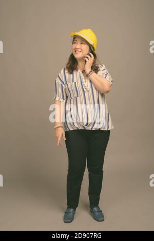 Reife schöne asiatische Geschäftsfrau trägt Hardhut vor grauem Hintergrund Stockfoto