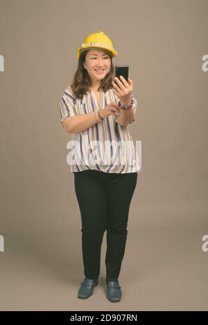 Reife schöne asiatische Geschäftsfrau trägt Hardhut vor grauem Hintergrund Stockfoto