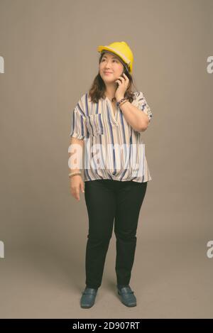 Reife schöne asiatische Geschäftsfrau trägt Hardhut vor grauem Hintergrund Stockfoto