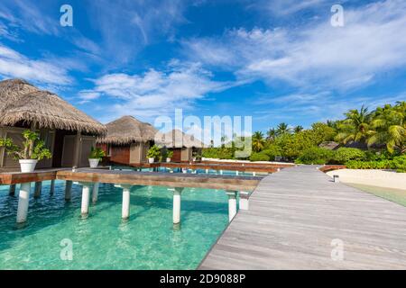 Water Villas Bungalows auf der perfekten tropischen Insel, wunderschöner weißer Sand am tropischen Strand blaues Wasser blauer Himmel mit Kokospalmen, Malediven Inseln Stockfoto