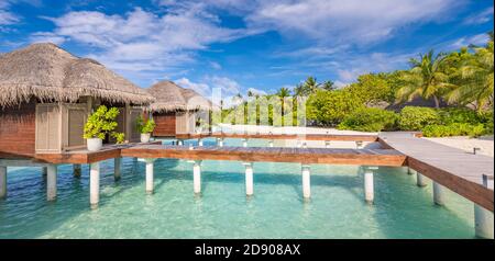 Water Villas Bungalows auf der perfekten tropischen Insel, wunderschöner weißer Sand am tropischen Strand blaues Wasser blauer Himmel mit Kokospalmen, Malediven Inseln Stockfoto