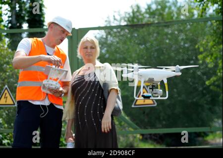 Quadcopter über dem Boden fliegen, männlicher Bediener hält Fernbedienung und Frau auf einem verschwommenen Hintergrund Stockfoto