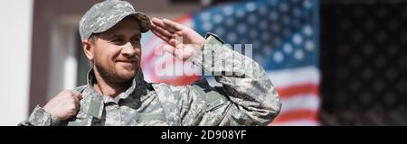 Lächelnder Militärangehörige mit verschwommener amerikanischer Flagge auf dem Hintergrund, Banner Stockfoto