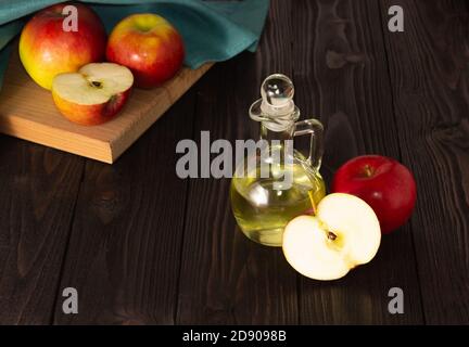 Apfelessig in einer Glasdekanter auf einem dunklen Holztisch. Äpfel in der Nähe. Stockfoto