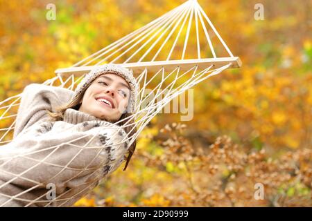 Glückliche Frau im Urlaub, die auf Hängematte ruhend, die Seite betrachtet Im Herbst in einem schönen Orangenwald Stockfoto