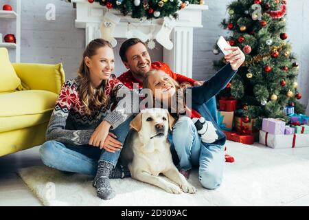 Mädchen, die Selfie mit fröhlichen Eltern und Hund in dekoriert Wohnzimmer Stockfoto