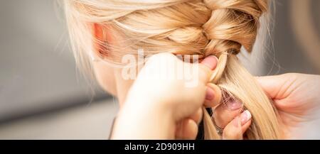 Nahaufnahme der Rückansicht der weiblichen Hände, die ein Zopf umflechten An junge blonde Frau im Schönheitssalon Stockfoto