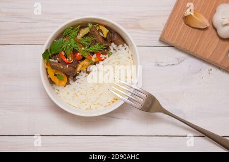 Roastbeef mit Paprika und weißem Reis. Weiße Platte, Knoblauch im Hintergrund. Blick von oben auf ein köstliches Gericht auf der Speisekarte. Stockfoto
