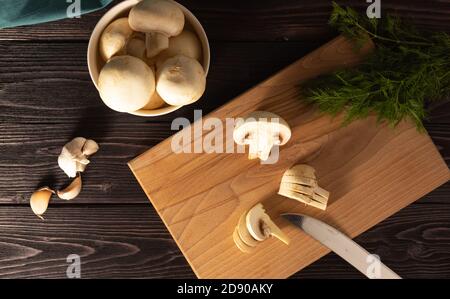 Gehackte Pilze auf einem Holzbrett. Dill, ganze Pilze im Hintergrund. Vegetarische Küche. Der Blick von oben. Stockfoto