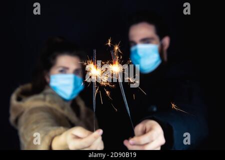 Junges Paar mit schützenden Gesichtsmasken für Coronavirus und mit Wunderkerzen für Silvester, 2021 und Covid-19 Konzept Stockfoto