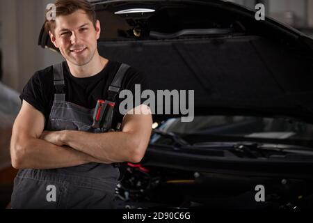 Portrait von stattlichen kaukasischen Auto Mechaniker Mann, in der Nähe der Autohaube in Auto-Service-Werkstatt, trägt Uniform Stockfoto