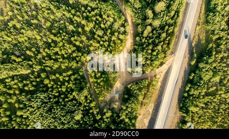 Luftaufnahme der Landstraße mit wenigen Autos fahren zwischen Wäldern an einem sonnigen Tag. Landschaftlich schöne Draufsicht von Drohne auf Naturlandschaft und Autobahn. Licht tr Stockfoto