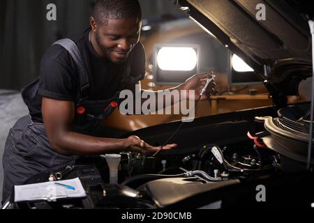 Professioneller Automechaniker prüft Motor unter der Haube an der Autowerkstatt, macht Notizen und prüft Notizen im Notizbuch Stockfoto