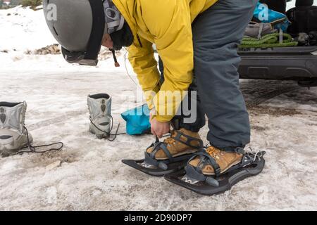 Ein sportlicher Mann zieht seine Schneeschuhe an, um einen verschneiten Bergausflug zu starten. Er liebt Wintersport Stockfoto