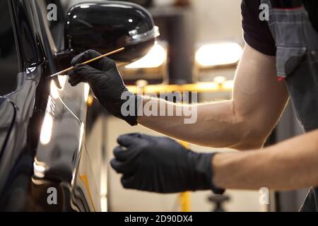 Cropped kaukasischen Auto-Service-Arbeiter ist Malerei Auto Details, verwenden Sie kleine Bürste und Farbe, gelten sie auf der Oberfläche des schwarzen Automobils Stockfoto