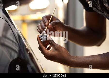 Junge afro Auto-Service-Arbeiter malt Auto-Details, verwenden Sie kleine Bürste und Farbe, gelten sie auf der Oberfläche des schwarzen Automobils Stockfoto