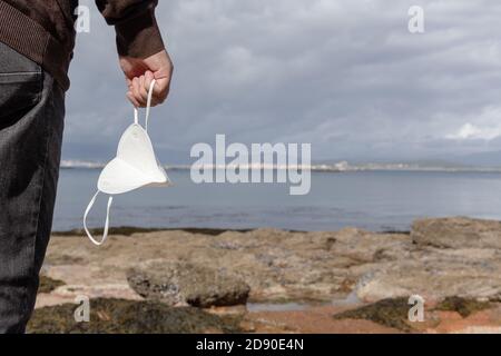 Männliche Hand hält an einem sonnigen Tag eine Gesichtsmaske an einem wilden Strand. Outdoor Freedom während Covid-19 Pandemiekonzept. Speicherplatz kopieren Stockfoto