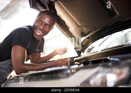 Fröhlich lächelnd afro Mann genießen Reparatur Auto Haube, überprüfen Sie die Details, behebt Maschinenprobleme Stockfoto