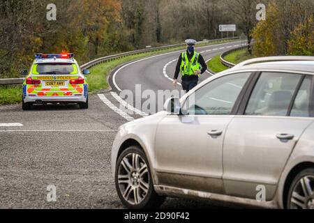 Walisische Polizei zieht Autos an einem Kontrollpunkt während Feuerbremsfahrzeuge Patrouillen nahe der Grenze zwischen Camarthenshire und Pembrokeshire, Wales. Erster Minister Mark Drakeford wird am Montag neue nationale Coronavirus-Maßnahmen für Wales vorstellen. Stockfoto