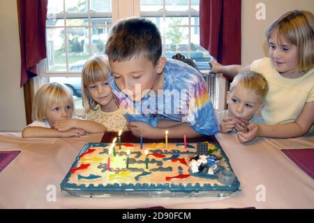 9-jähriger Junge feiert Geburtstag mit Party mit Freunden Durch das Teilen von Geschenken und einem Kuchen mit Kerzen Stockfoto