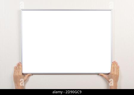 Frau Hände halten silbernen leeren Rahmen. Mockup Rahmen für das Bild von Zertifikat, Diplom oder Foto. Frau hängen Fotorahmen mockup an der grauen Wand Stockfoto