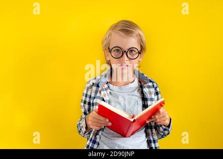 Portrait von niedlichen und cleveren blonden kaukasischen Jungen in einem karierten Hemd auf gelbem Hintergrund. September Tag. Bildung und zurück zur Schule Konzept. Kind Stockfoto