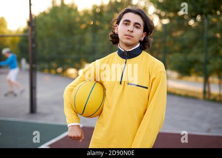 Portrait des Sportlers Junge mit Ball, Kerl kam, um Basketball nach dem Universitätsunterricht zu spielen, Ruhe haben, genießen Stockfoto