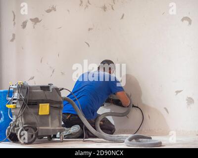 Arbeiter glättet die Wand mit Maschinen mit Maske Stockfoto