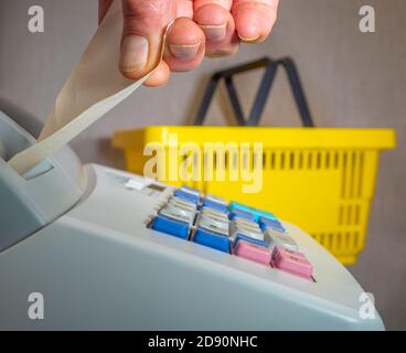 Schließen Sie die POV-Aufnahme eines Mannes, der ein Stück Papierrolle auf einer Ladenkasse abreißt, mit einem gelben Warenkorb im Hintergrund. Stockfoto