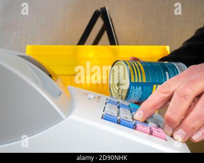 Nahaufnahme POV Aufnahme eines Mannes Hand hält eine Dose aus einem gelben Kunststoff-Warenkorb, während die Eingabe des Preises auf einem Shop / Shop Kasse bis. Stockfoto