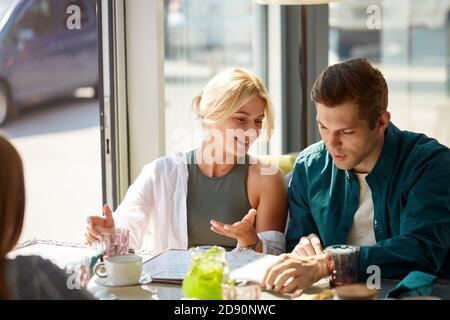 Glückliches junges Paar genießen, während die Auswahl einer Bestellung von der Speisekarte im modernen Café, sie diskutieren Mahlzeit, was zu bestellen Stockfoto