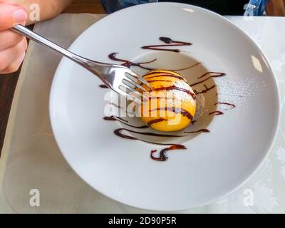 Nahaufnahme einer Gabel, die in ein gebratenes Eis-Dessert in einem Gericht klebt. Flach liegend, Draufsicht. Typisch chinesischer Kuchen. Stockfoto