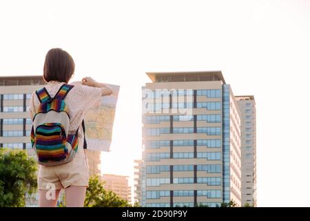 Rückansicht einer jungen Touristenfrau mit Rucksack auf einer Karte vor der Stadt, Konzept der Jugend und Reisenden Lebensstil, Copy Platz für Text Stockfoto