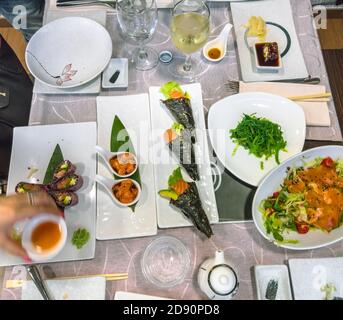 Flaches Lay von einem japanischen und chinesischen Fusion-Tisch voller köstlicher Gerichte. Schwarzer Uramaki aus Lachs, Temaki-Reiszapfen, frischer Lachstartar, Seetang Stockfoto